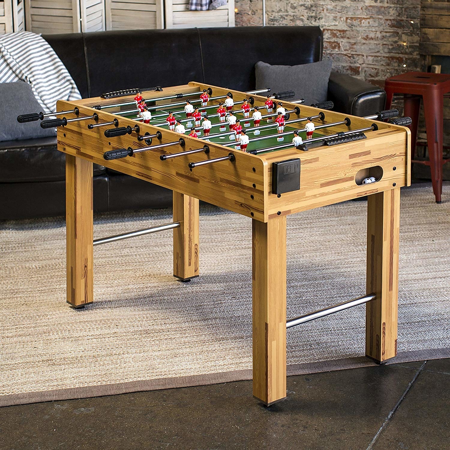the foosball table  which has four legs and bars sticking into the top of the table that can be spun to control the soccer men on the bars inside of the table