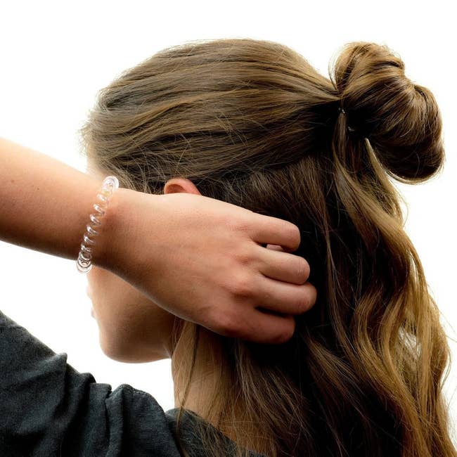 Model with with her hair half up and a clear spiral hair tie around her wrist 