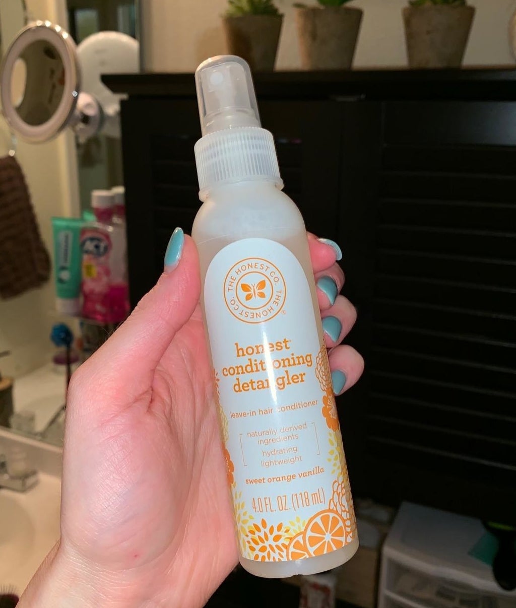 A hand holding the detangler spray bottle, which is about the size of a body spray or face mist 