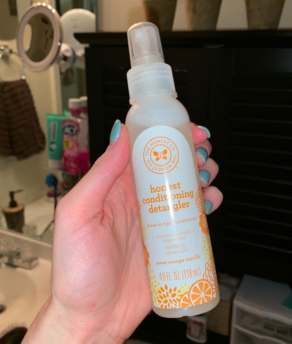 A hand holding the detangler spray bottle, which is about the size of a body spray or face mist 