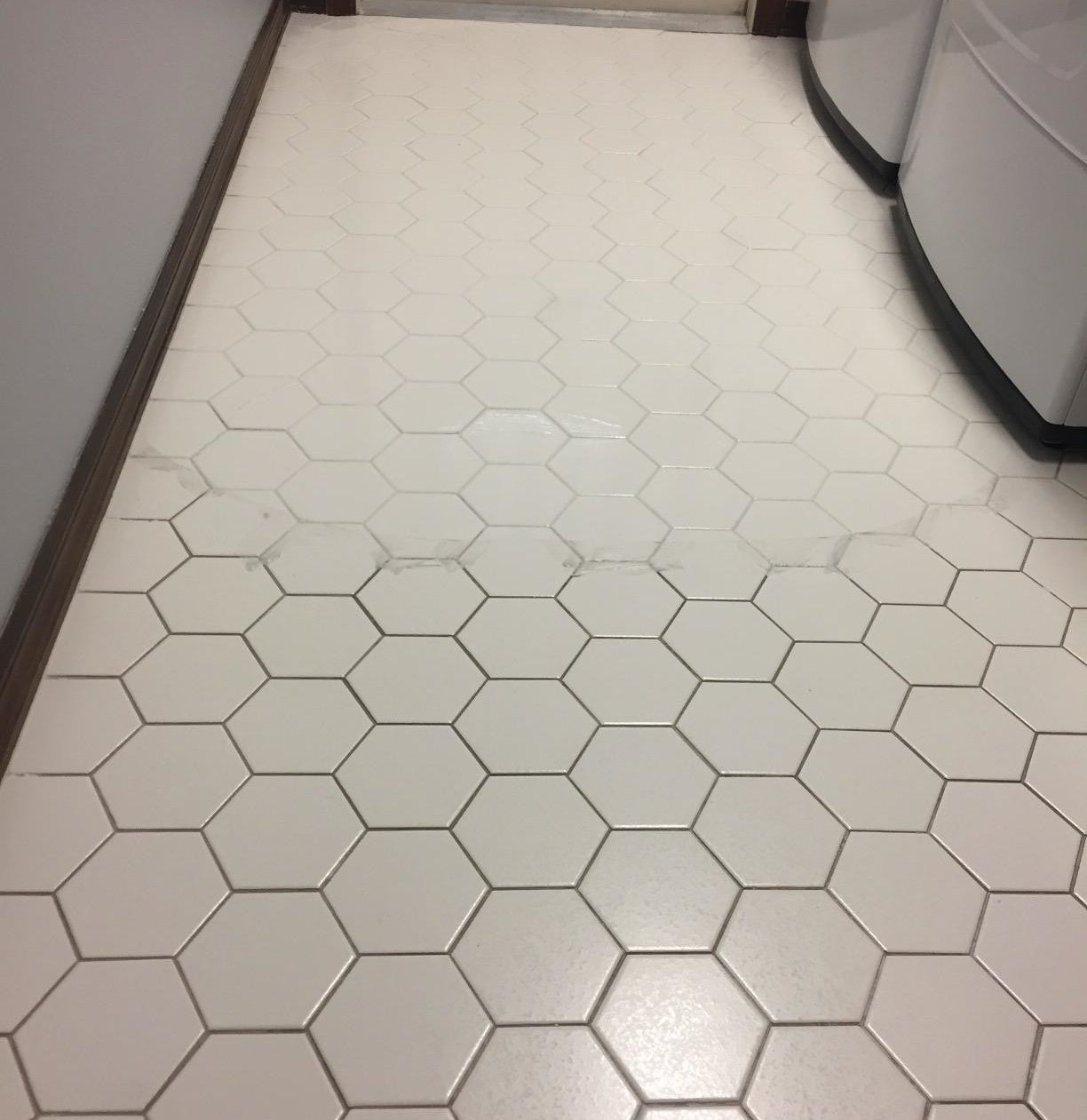 A tiled floor that has been scrubbed and now looks much brighter, whiter, and cleaner than the section of the floor that has not yet been scrubbed 