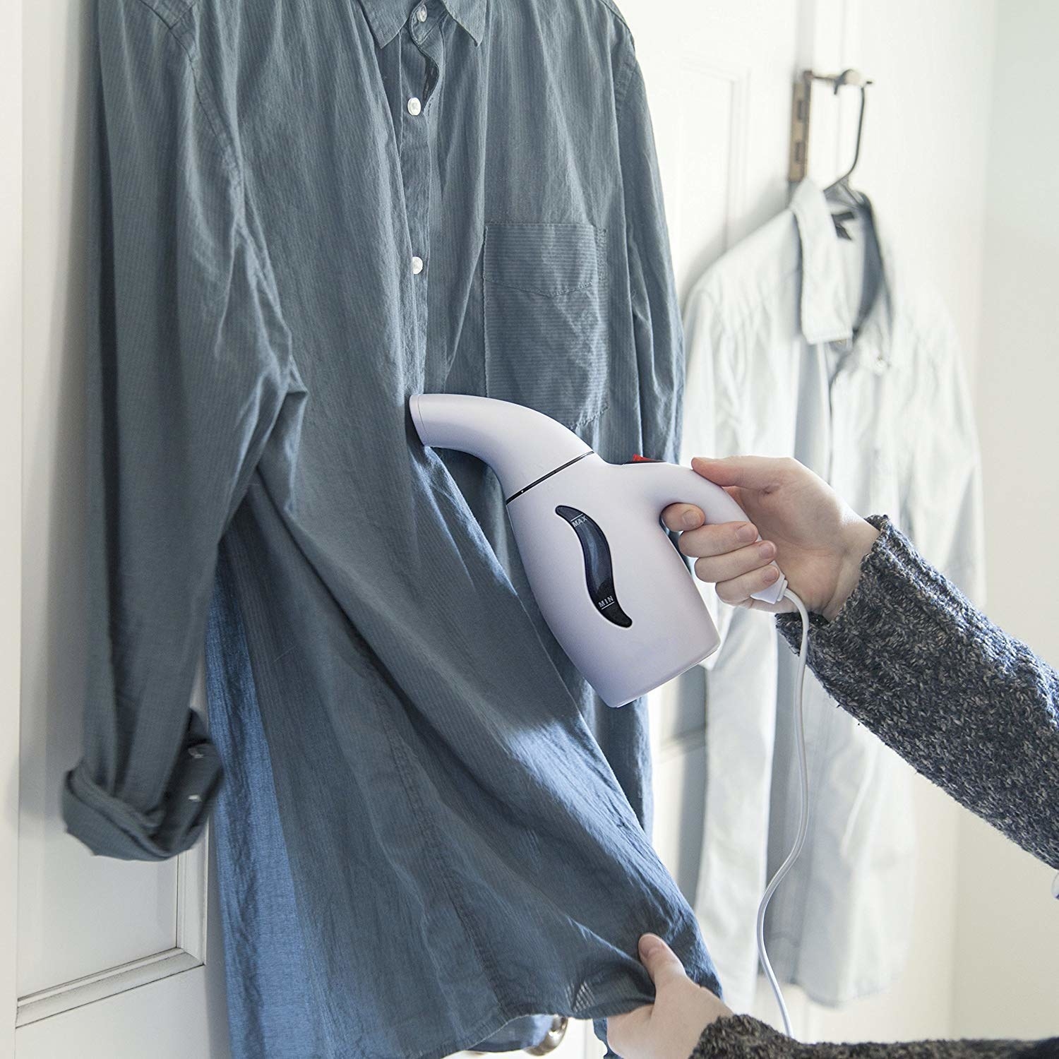 A person using a small handheld steamer on their button up shirt