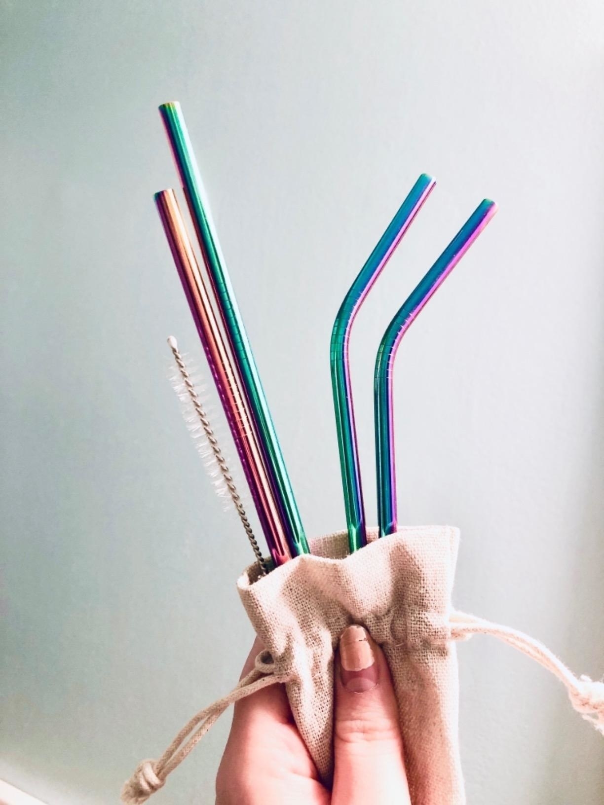 a hand holding a beige pouch containing rainbow steel straws