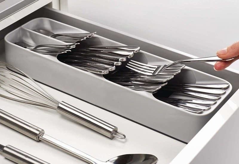 A person putting a fork inside the cutlery organizer inside the drawer