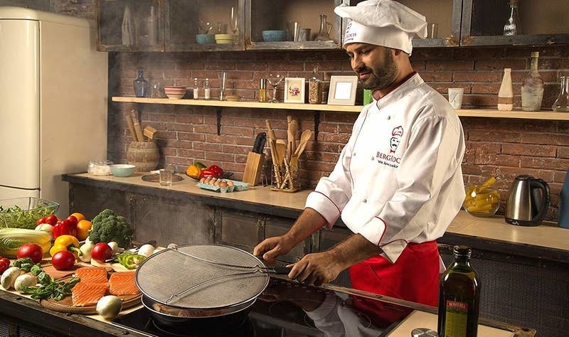 a chef holding the splatter screen over the frying pan 