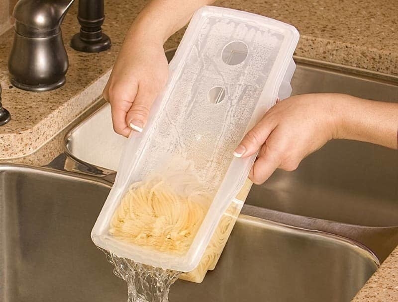 A person dumping water out of the container and into the sink while the pasta stays securely inside 