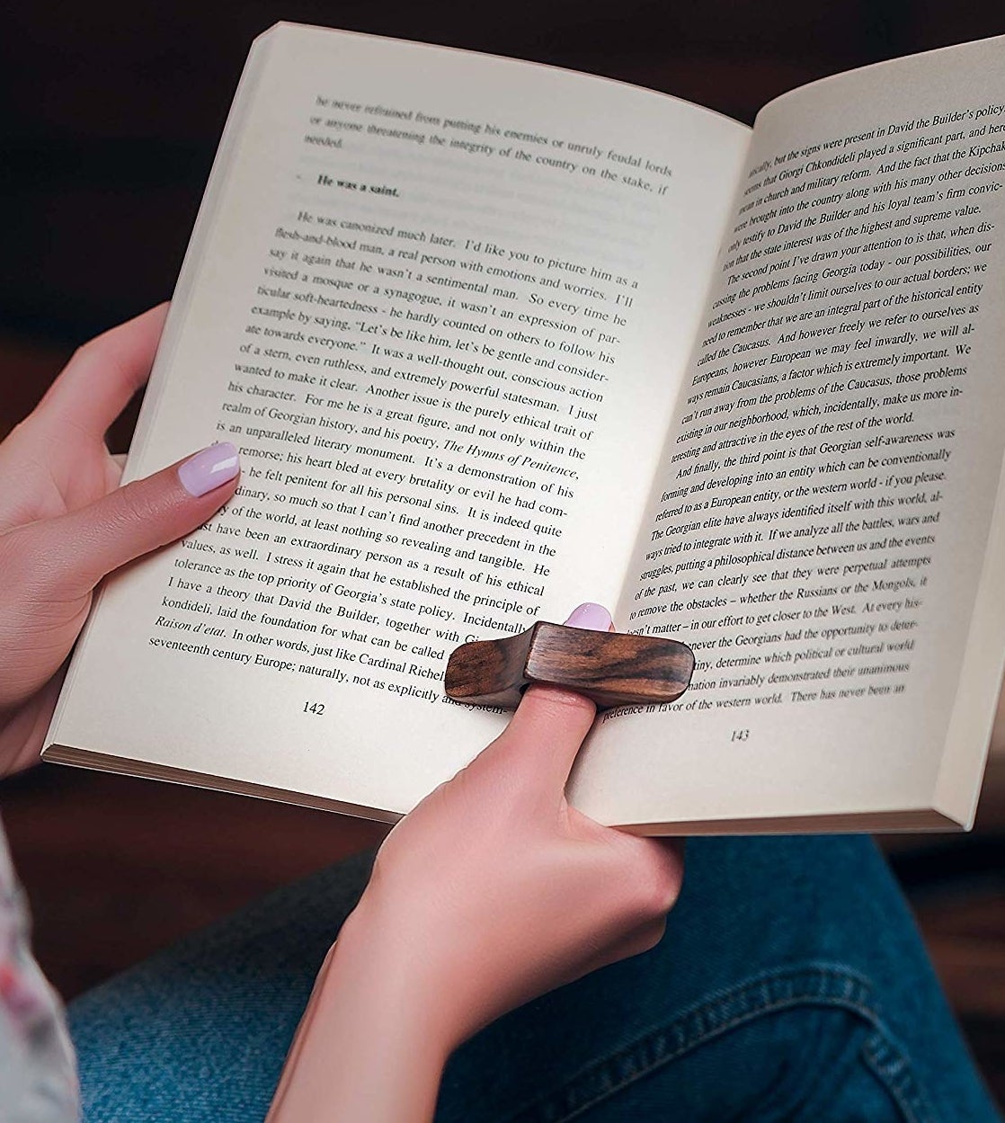 Someone wearing the wooden page holder to prop open their book while reading