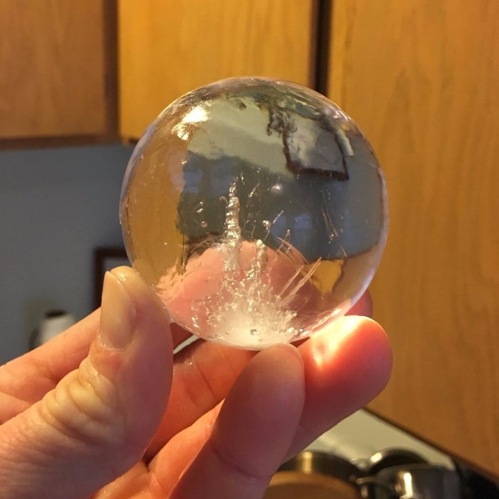 A hand holding a solid ice sphere