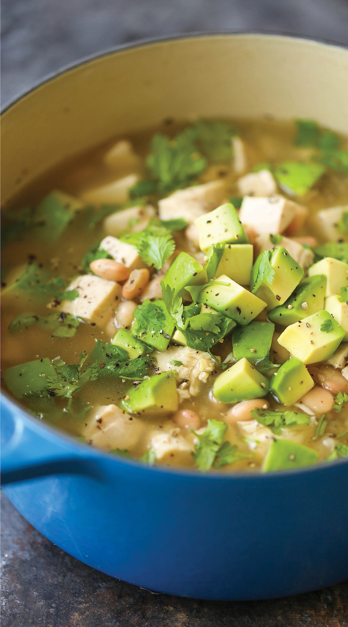 A pot of hearty soup featuring chunks of avocado, white beans, diced chicken, and garnished with fresh cilantro