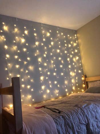 The string lights draped down a wall by a bed in the dark