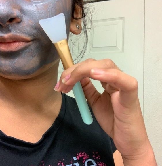 Reviewer using the brush to apply a charcoal face mask 