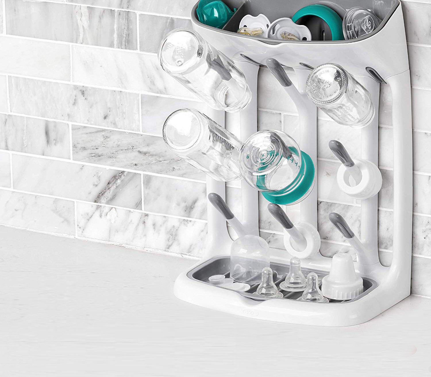 An upright dish rack with multiple hooks and a shelf above them The hooks have baby bottles hanging from them with pacifiers lying in the shelf