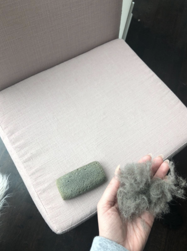 reviewer holding a handful of cat hair beside of a fur-free chair