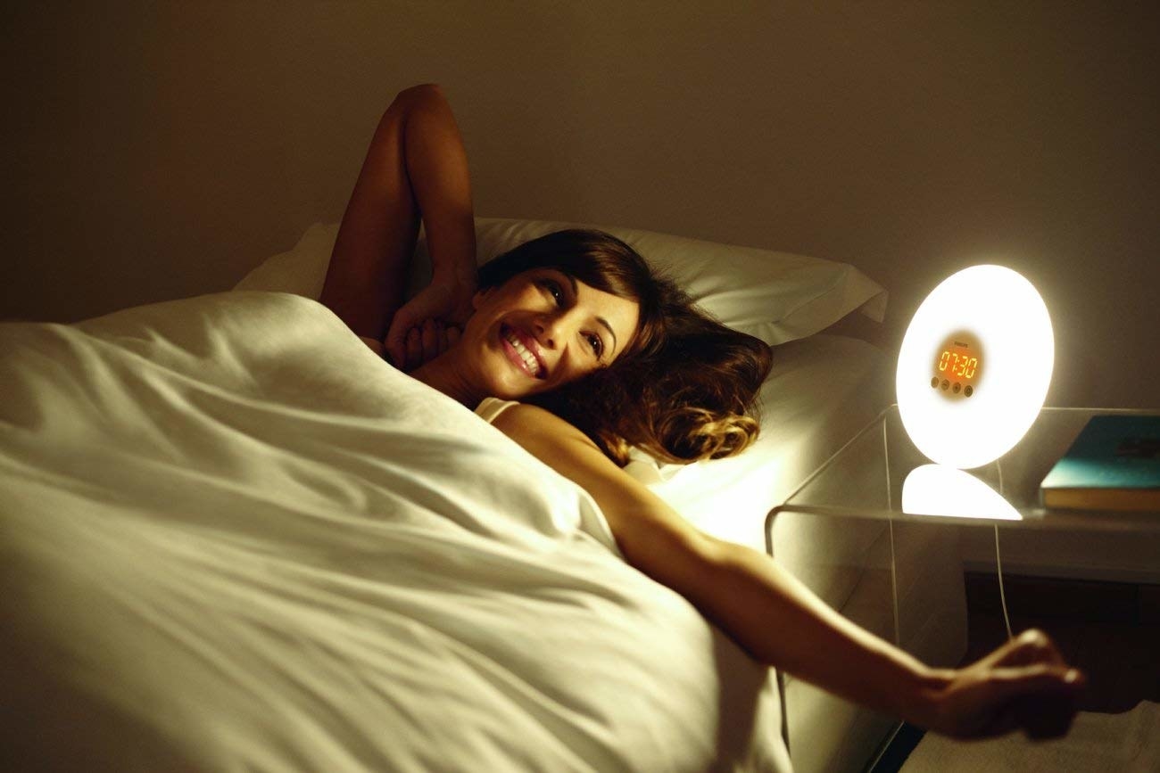 a model stretching in bed near the glowing sunrise alarm clock 