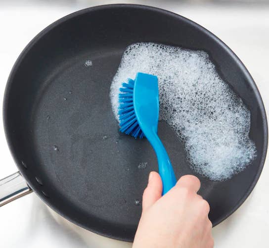 A person cleaning a pan with a blue dishwashing brush.