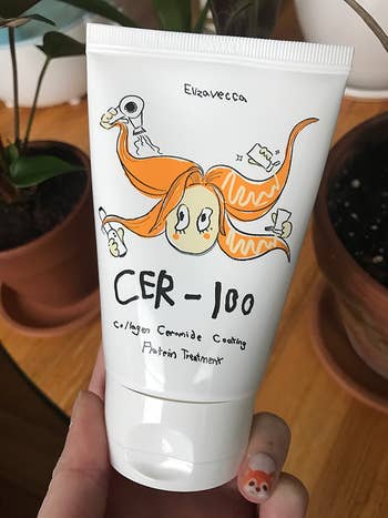 pic of Bek holding white container of the collagen-coating hair treatment with a cute illustration on the front