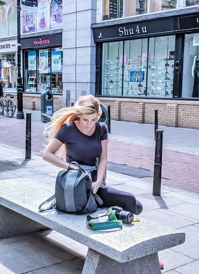 reviewer sitting on a bench with the grey backpack with lighter grey stripe down the middle