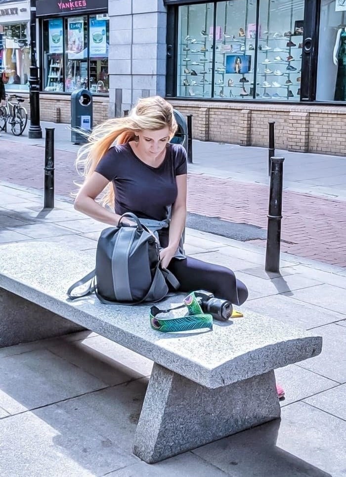reviewer sitting on a bench with the grey backpack with lighter grey stripe down the middle