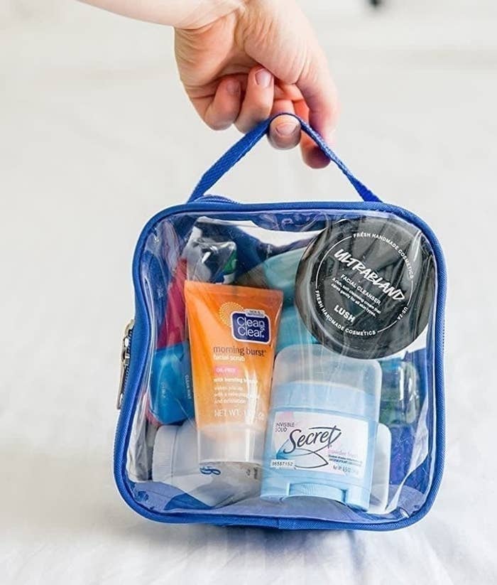 hand holding the clear square bag with blue trim filled with toiletries