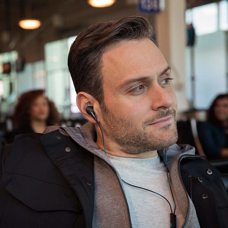 model with the black earbuds in while sitting in what looks like an airport