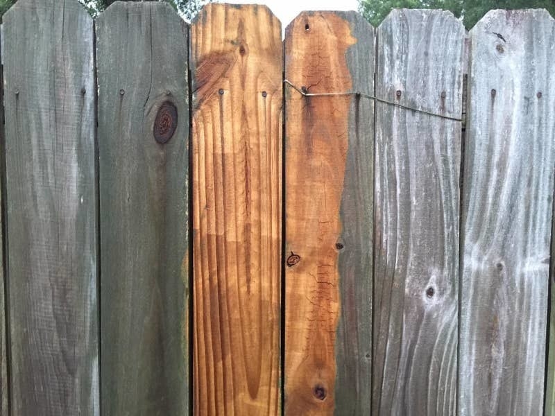 reviewer&#x27;s before-and-after of their wood fence looking dirty and gray compared to a section looking clean and wooden brown again 