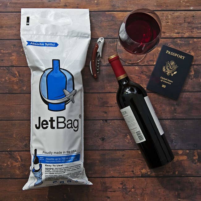the white plastic bottle bag with a bottle of wine, wine glass, bottle opener, and passport next to it