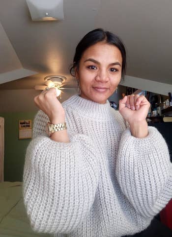 reviewer showing off the sleeves of the sweater in gray