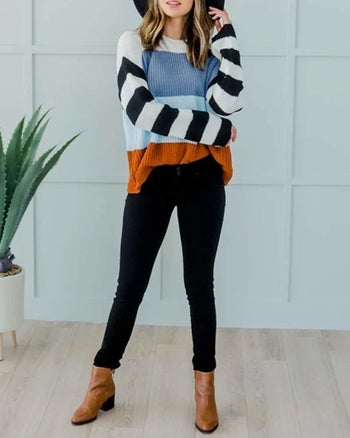 A model wearing the pullover sweater with color blocking and black and white striped sleeves