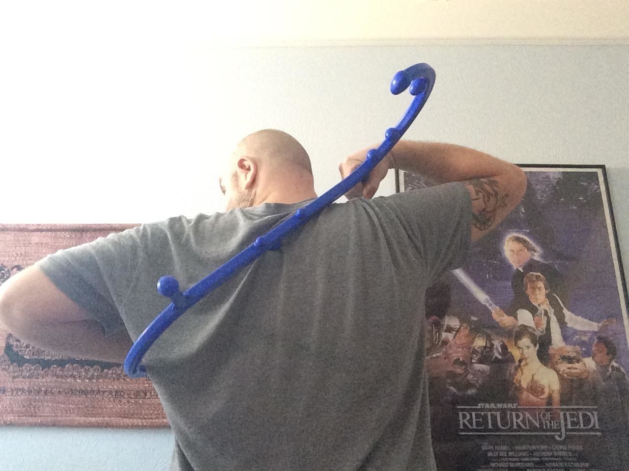 reviewer using the s-shaped stick across their back with little knobs all over it