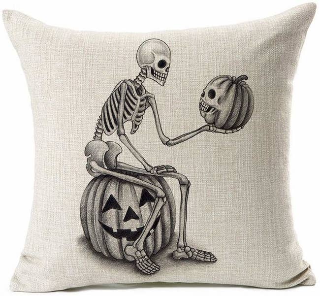 a gray pillow cover with a skeleton sitting on a jack o lantern and holding + looking at another smaller pumpkin with a skeleton face