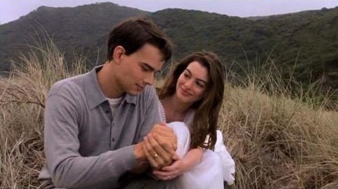 Anne Hathaway and Christopher Gorham sit on a hill