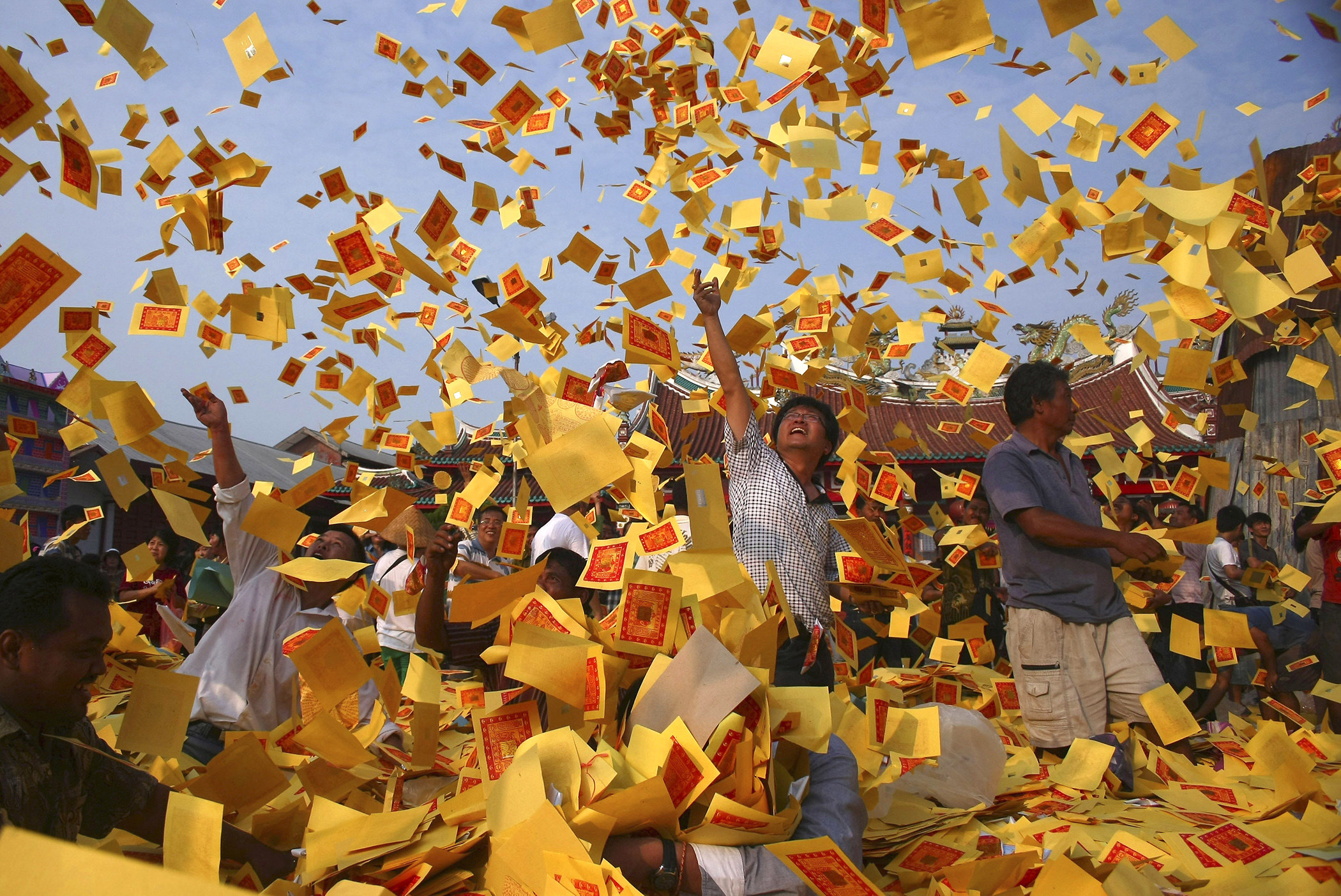 People in an East Asian temple throw yellow pieces of paper with red stamps on them into the air
