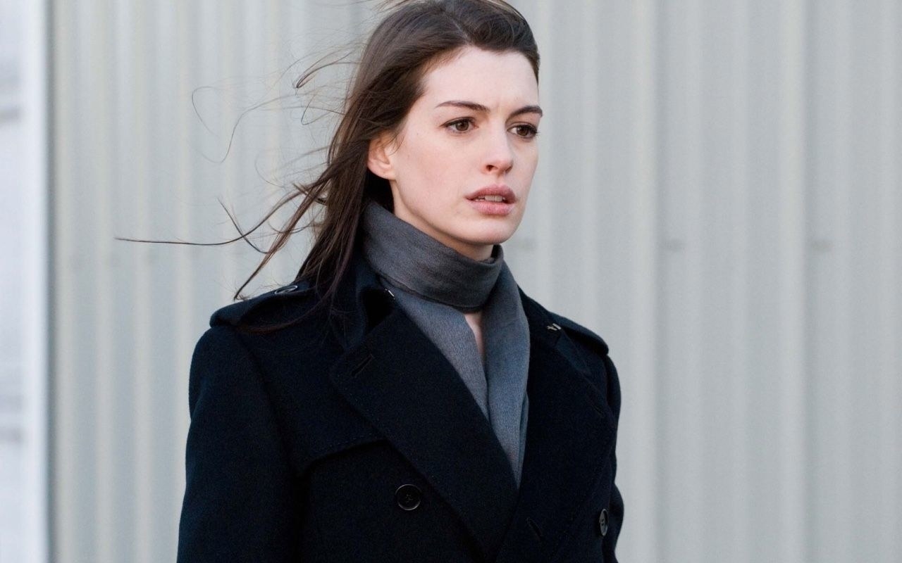 Anne Hathaway stands in a scarf and jacket