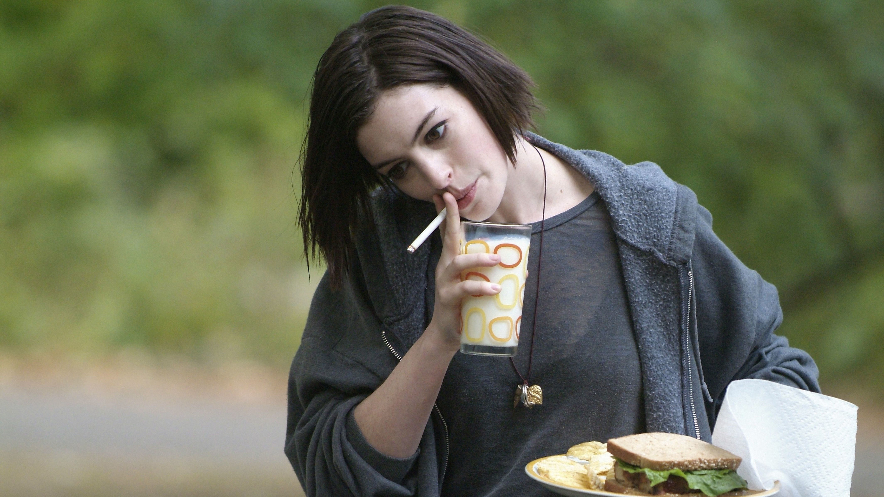 Anne Hathaway smokes and caries a plate with a sandwich on it