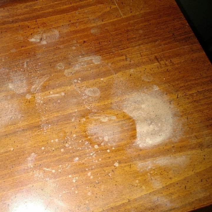 reviewer's photo of a wooden table with a lot of marks and stains on it 