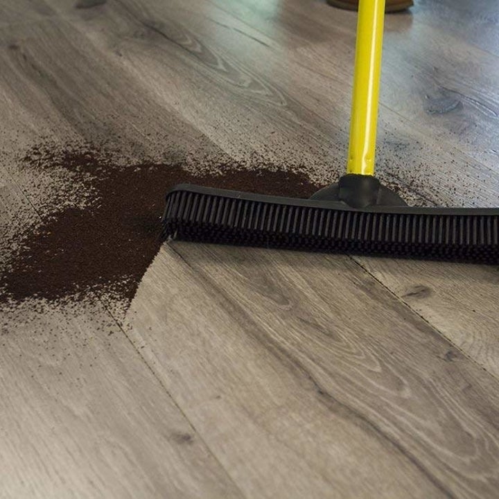 the broom sweeping up coffee grounds from a hardwood floor 