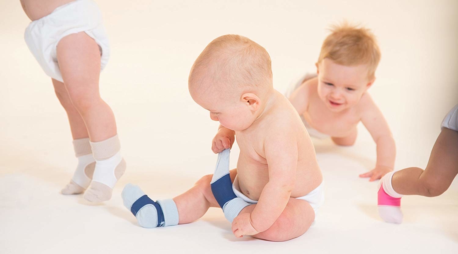 several babies wearing socks and diapers. one is unsuccessfully trying to remove a sock that has the product covering it.