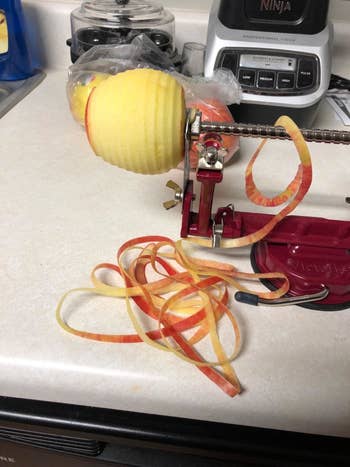A reviewer uses the device to peel off an apples skin in a thin, long spiral strip