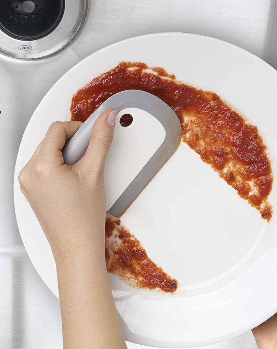 Dish squeegee cleaning tomato sauce off plate 