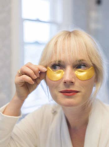 model applies gold eye masks to face
