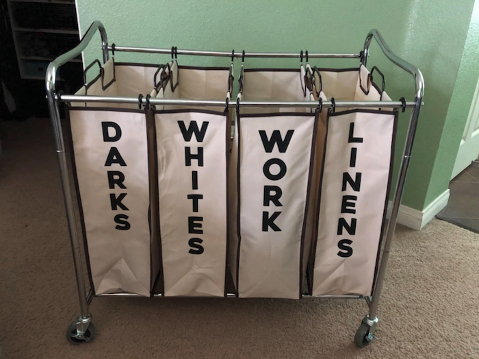 four fabric bags shaped like squares and hanging from a metal frame which is on wheels. The bags read &quot;darks,&quot; &quot;whites,&quot; &quot;work,&quot; and &quot;linens&quot; from left to right.
