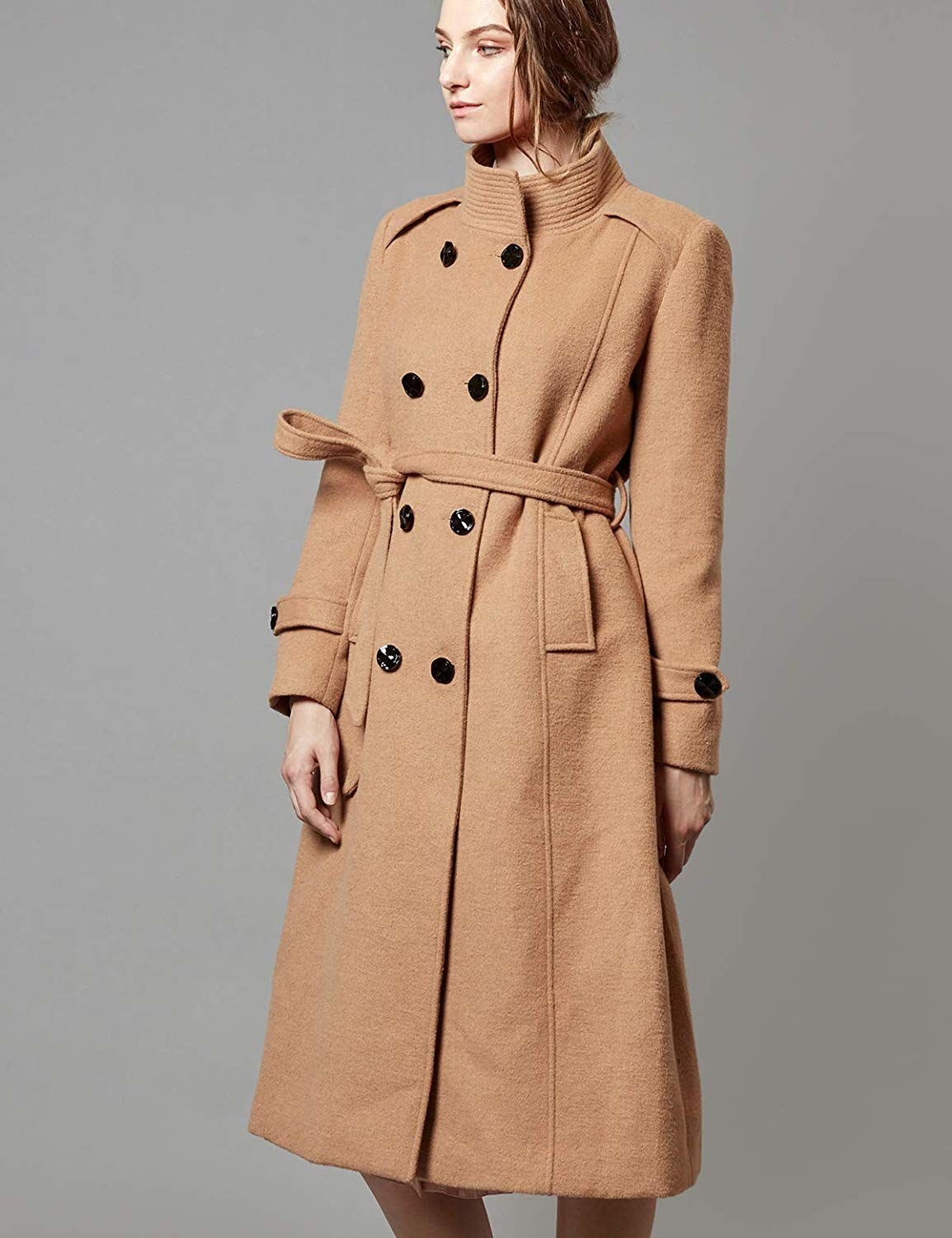Model wearing the below knee-length coat in tan with two rows of black buttons down the center
