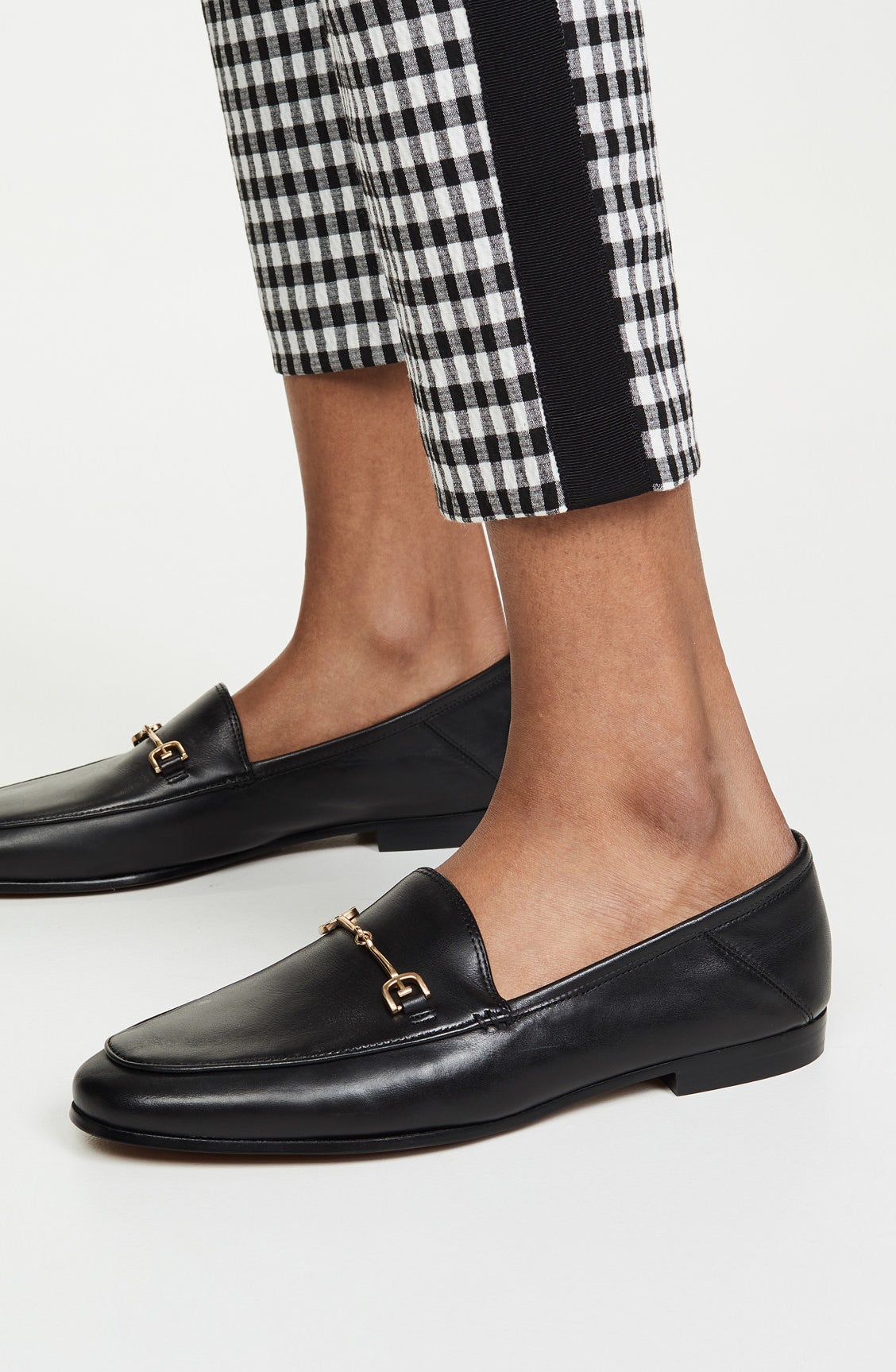 The loafers in black with a small gold metal bar across the top