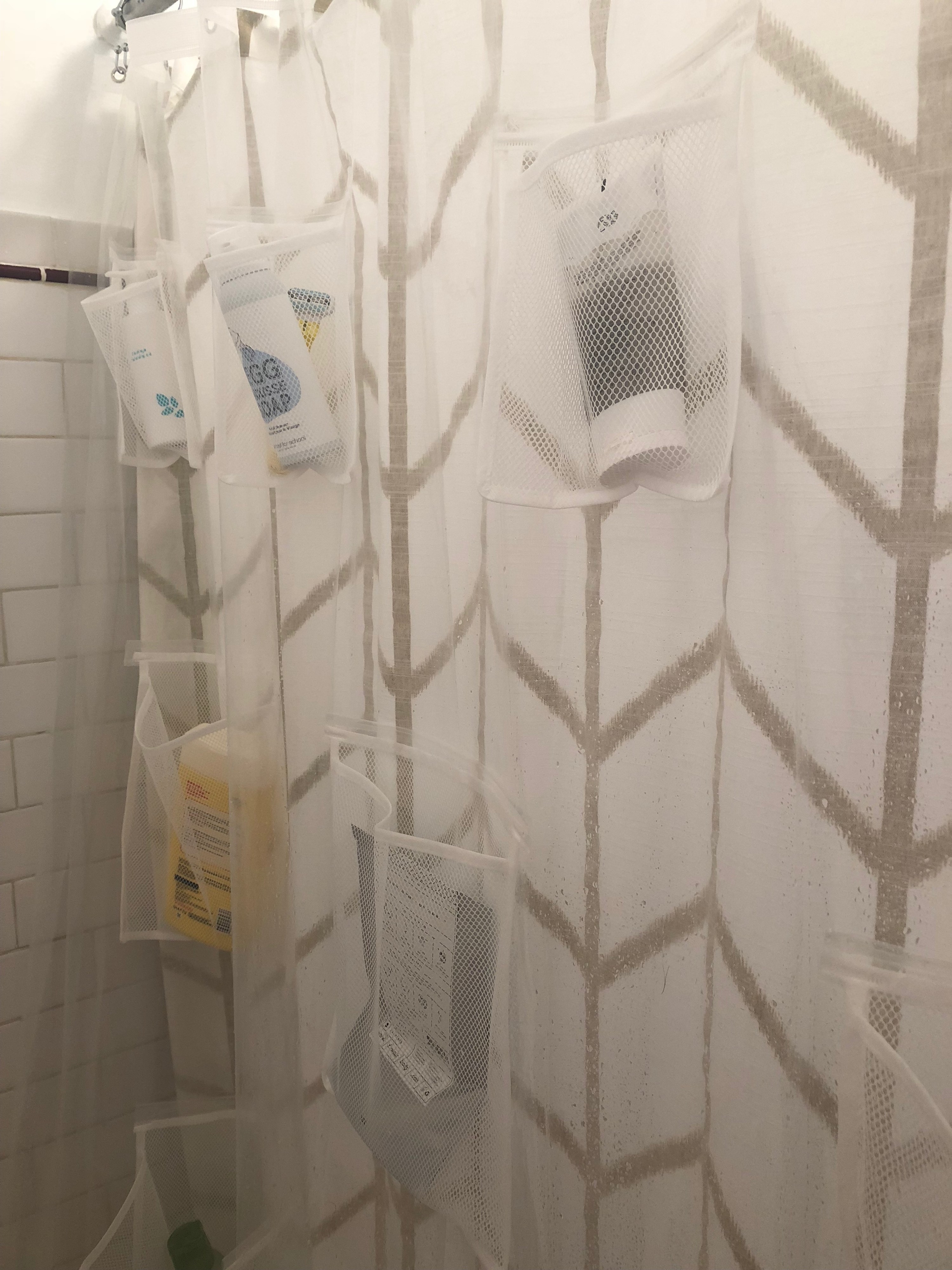 shower with the translucent shower curtain liner hanging up. Various toiletries like shampoo and body wash are in its mesh storage pockets