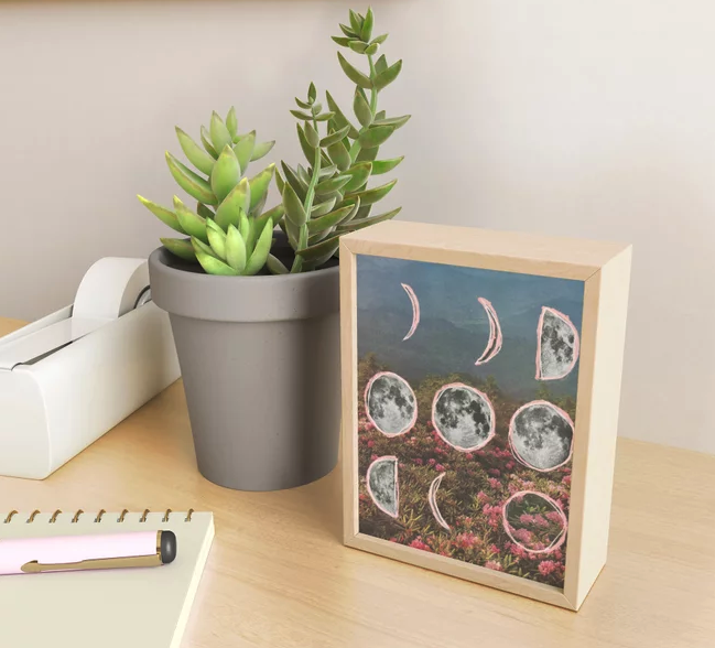 the print featuring a field of flowers, mountains, and illustrated phases of the moon