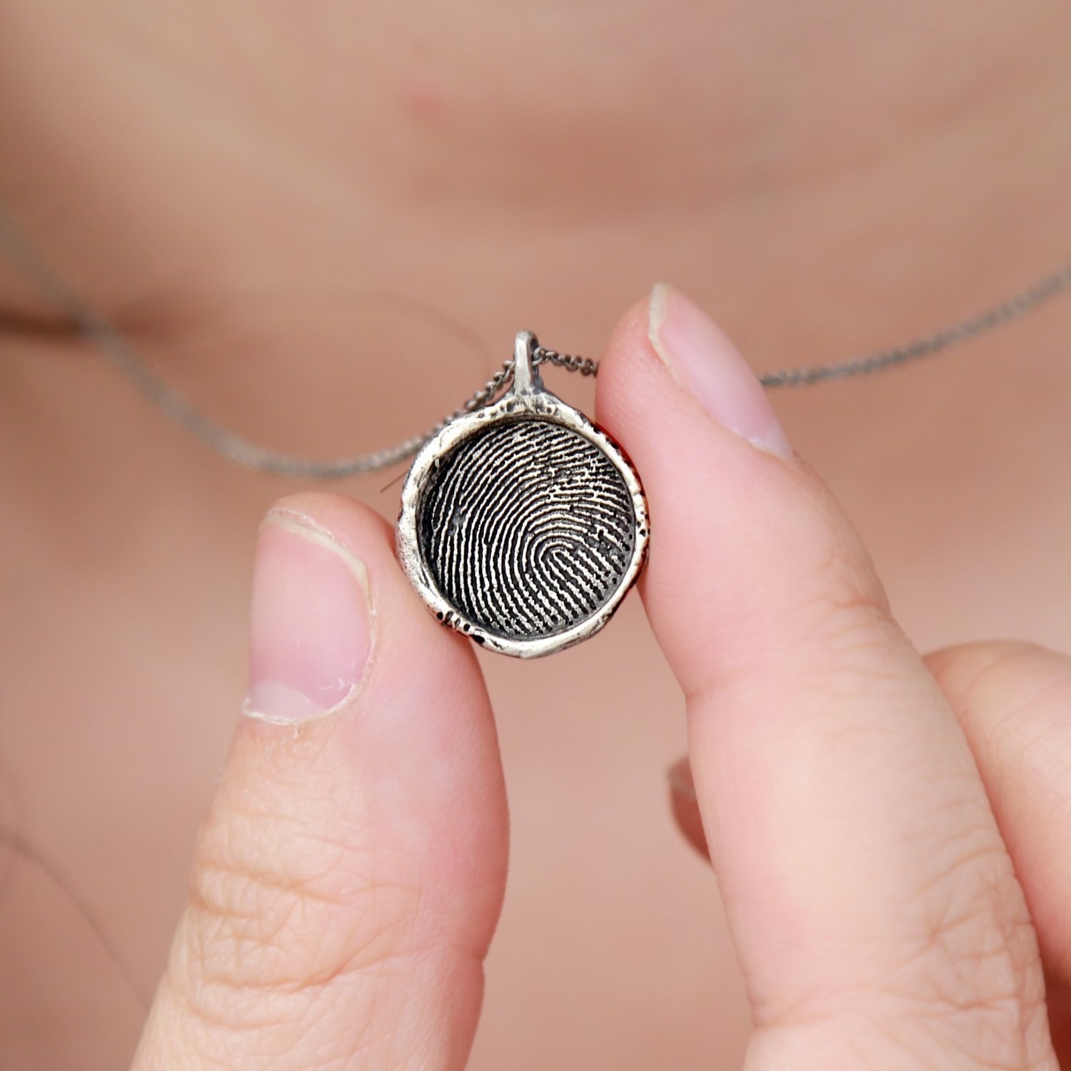 A person holding up a circular necklace charm with a fingerprint engraved in it