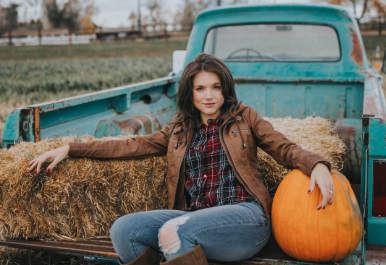 a reviewer wearing the brown jacket over a flannel in the bed of a pick up truck with a pumpkin