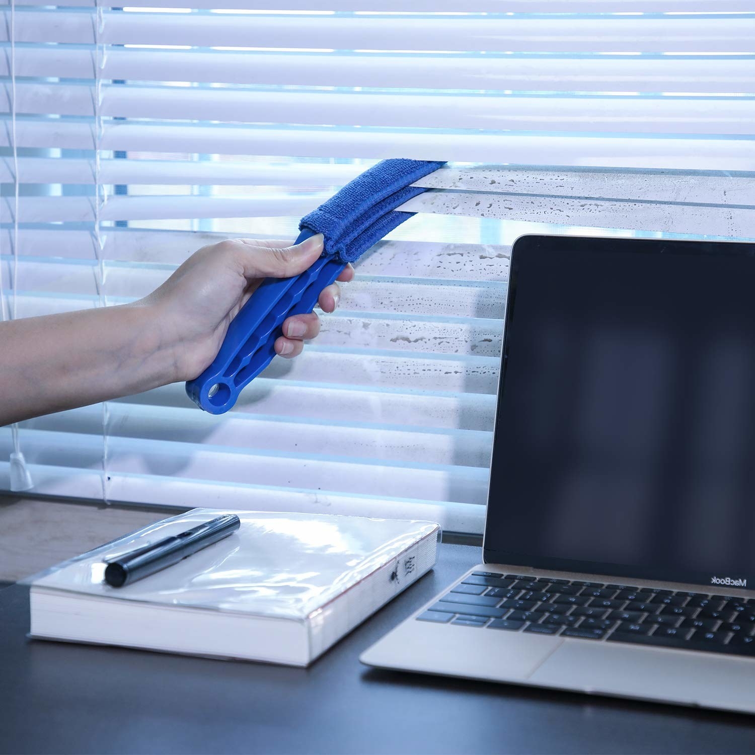 A person cleaning dust off their blinds with a small brush that has three layers of microfibre cloth on it