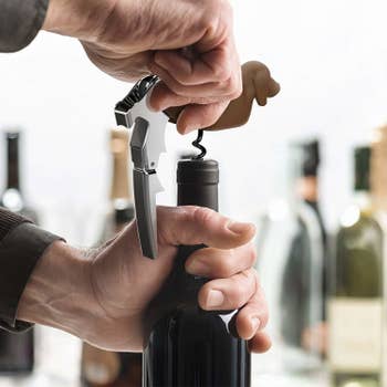 A model flipping the bottom of the dachshund to reveal a corkscrew they're using to open a bottle of wine