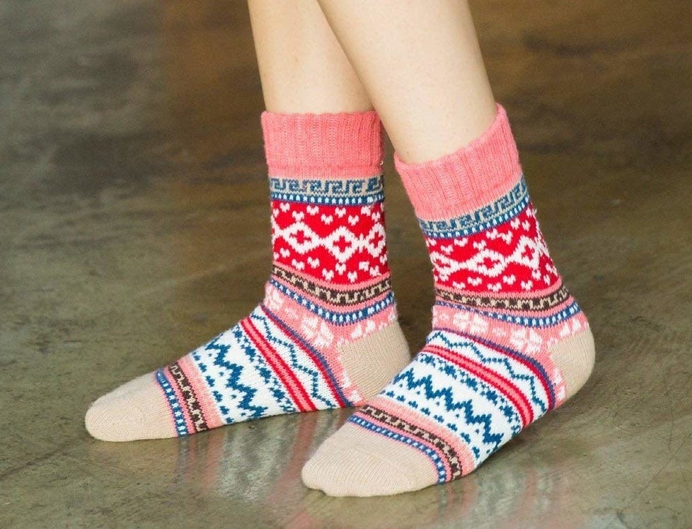 A model wearing the socks with a pink, red, brown, white, and blue Christmas sweater pattern